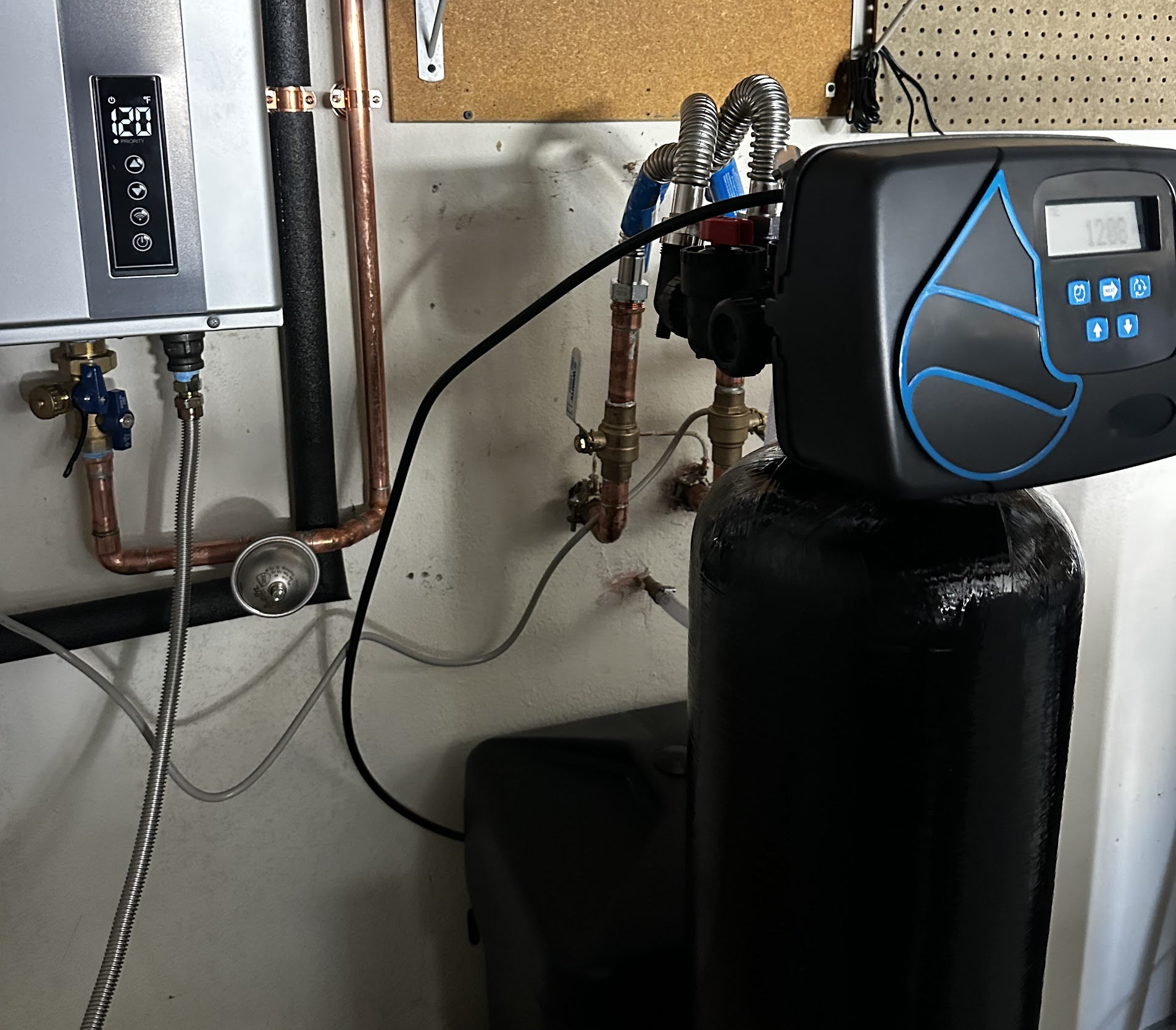 A black water softener tank with a digital control head and a tankless water heater mounted on a utility wall in a Las Vegas home.
