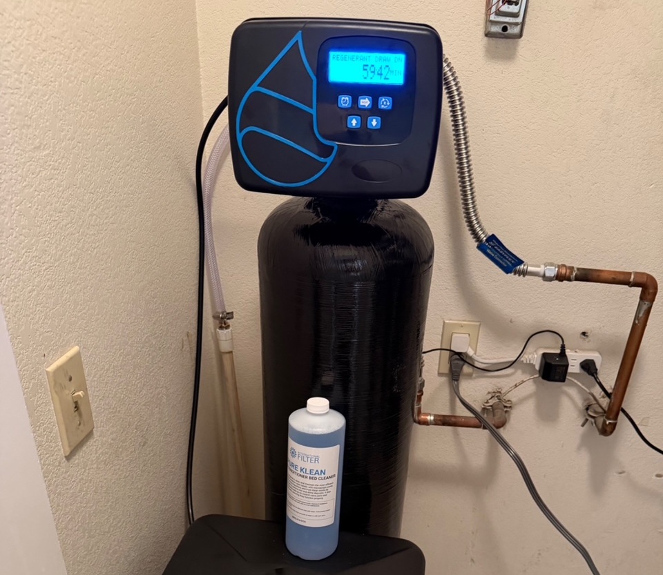 A whole-house water softener control head showing regeneration status and a bottle of filter bed cleaner in a Las Vegas utility space.